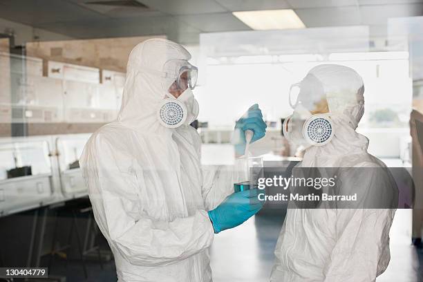 scientists in protective gear putting liquid in beaker in lab - 防護服 個照片及圖片檔