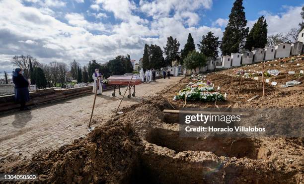 Nun and gravediggers wearing protective gear stand by as a priest prays over a plastic-covered coffin of a COVID-19 victim before burial at Cemitério...