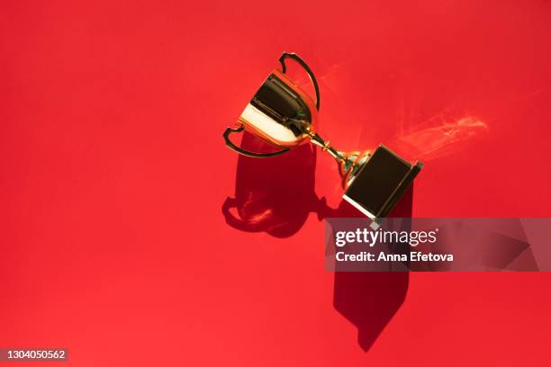 top view of metallic golden goblet on bright red background with shadow. goal achievement concept. trendy colors of the year - first light awards stock-fotos und bilder