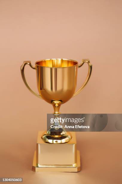 front view of metallic golden goblet on beige background. goal achievement concept - first light awards stock-fotos und bilder