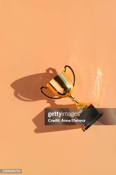top view of metallic golden goblet on beige background with shadow. goal achievement concept - winners podium imagens e fotografias de stock