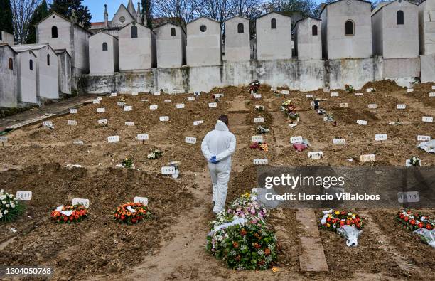 Gravedigger wearing protective gear walks among fresh graves in between burial of COVID-19 victims at Cemitério do Alto de São João during the...