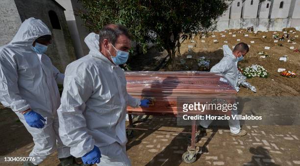 Gravediggers wearing protective gear transport a plastic-covered coffin of a COVID-19 victim before burial at Cemitério do Alto de São João during...