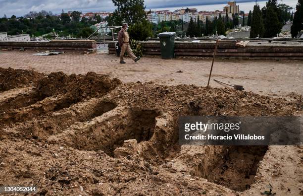 Cemetery employee wearing a protective mask walks by freshly-dug graves before the burial of a COVID-19 victim at Cemitério do Alto de São João...