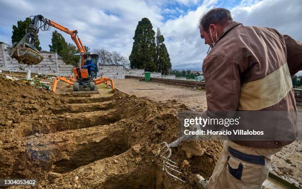 Cemetery employees operates a mechanical grave digger while a colleague finishes a gravesite at Cemitério do Alto de São João during the COVID-19...