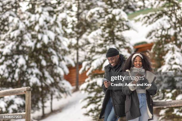 happy and attractive and stylish couple engage their smart phones outside in a winter setting - fun lovers unite stock pictures, royalty-free photos & images
