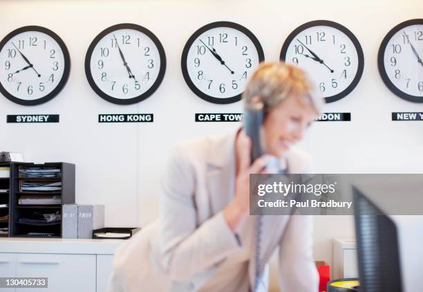 world clocks behind businesswoman in office - time zone stock pictures, royalty-free photos & images
