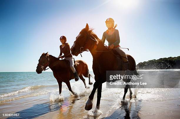 girls riding horses on beach - horse riding stockfoto's en -beelden