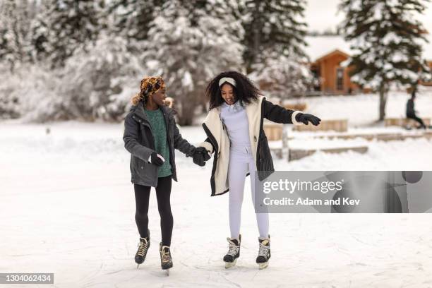 women hold hands for balance as they learn to ice-skate on frozen lake - ijsschaatsen stockfoto's en -beelden
