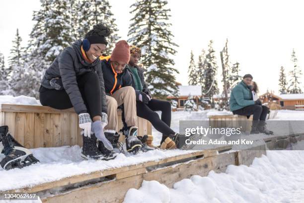 family laces up ice skates at outdoor ice rink - ice skating fotografías e imágenes de stock