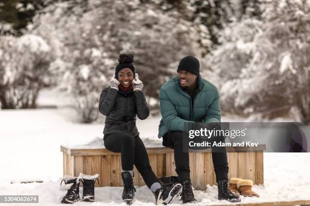 attractive couple sit at edge of frozen lake and contemplate ice-skating - wintersport stock pictures, royalty-free photos & images