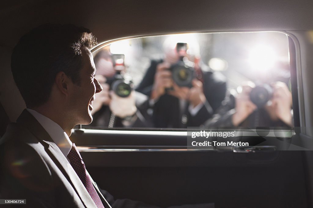 Politician smiling for paparazzi in backseat of car