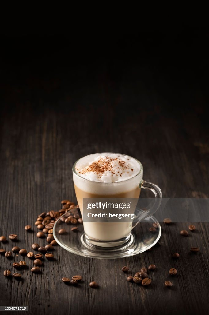 Latte Macchiato Kaffee geschichtet mit Milch, geröstete Kaffeebohnen auf schwarzem Holzhintergrund