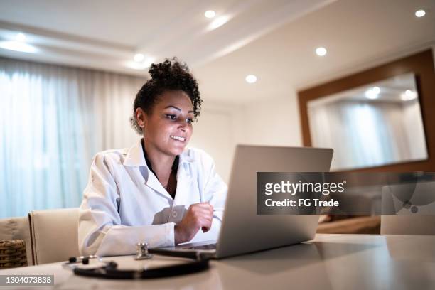 female doctor using laptop on a telemedicine call at home - telehealth visit stock pictures, royalty-free photos & images