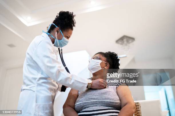 arts die aan de hartslag van de patiënt tijdens huisbezoek luistert - dragend gezichtsmasker - face mask protective workwear stockfoto's en -beelden