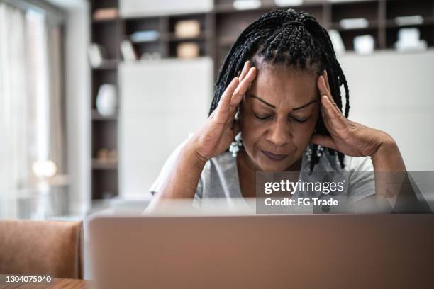 mature woman with headache in front of laptop at home - emotional stress home stock pictures, royalty-free photos & images