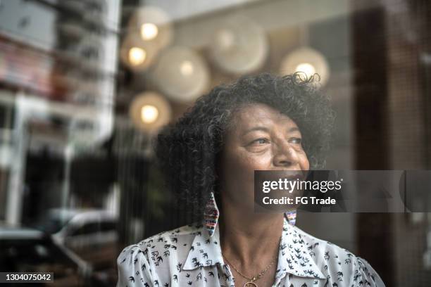 senior woman looking through the window at home - worry free stock pictures, royalty-free photos & images