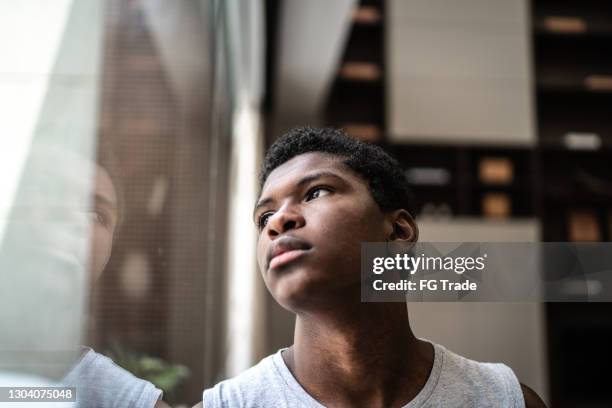 garçon d’adolescent regardant par la fenêtre à la maison - jeunes garçons photos et images de collection