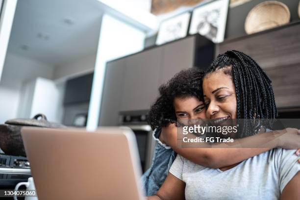 mature woman working from home and being embraced by daughter - 50 watching video stock pictures, royalty-free photos & images