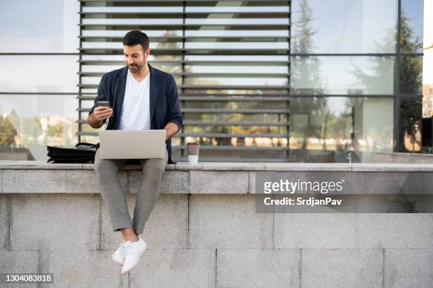 junger mann schaut auf sein handy, während er draußen arbeitet - business talk sit men stock-fotos und bilder