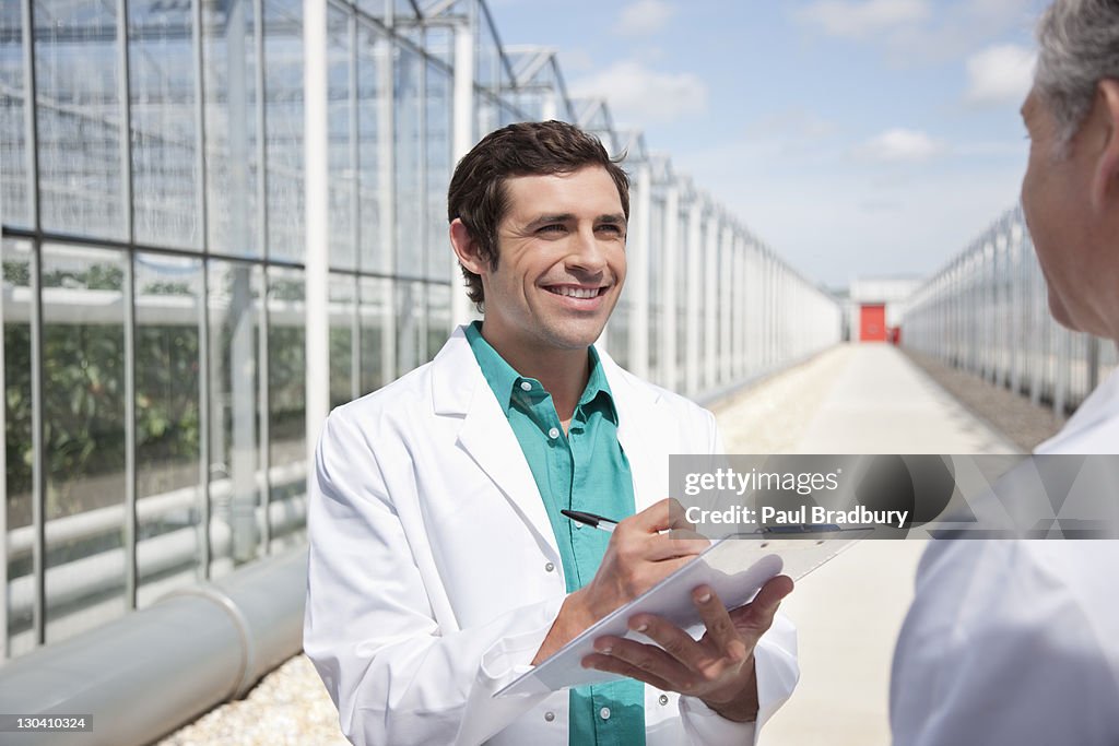 Scientist writing on clipboard outside greenhouses