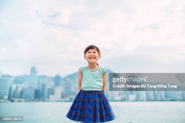 lovely little girl smiling & looking up to the sky joyfully by the promenade in the city - kid looking up to the sky imagens e fotografias de stock
