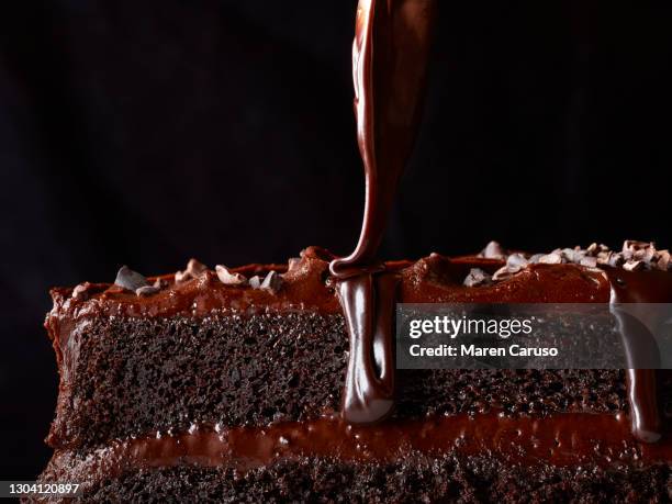 close up of chocolate sauce drizzling onto slice of chocolate cake - triefen stock-fotos und bilder