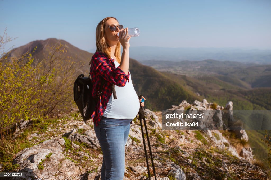Young pregnant woman drinking water in the mountain walks