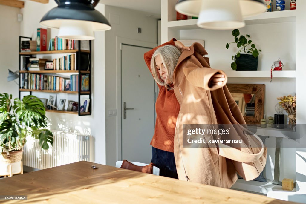 Senior Woman Putting on Coat Before Leaving Home