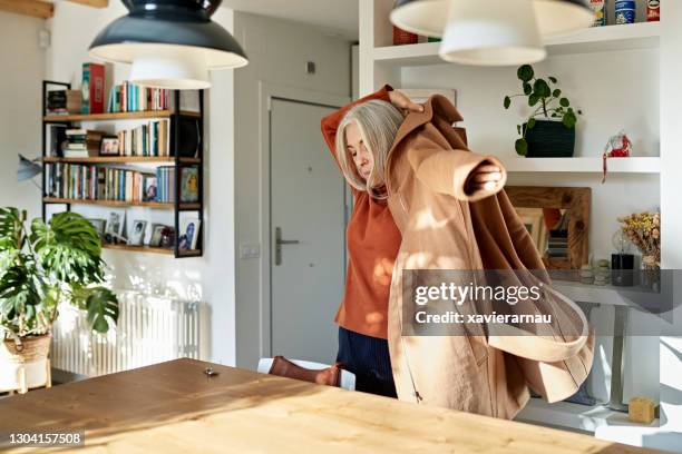 senior woman putting on coat before leaving home - calçada imagens e fotografias de stock