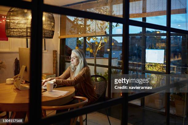 focused working senior typing on computer in home office - balcony window stock pictures, royalty-free photos & images