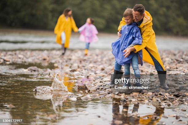 glücklicher vater lehrt seinen sohn, wie man steine in den fluss an regnerischen tag zu überspringen. - skimming stones stock-fotos und bilder