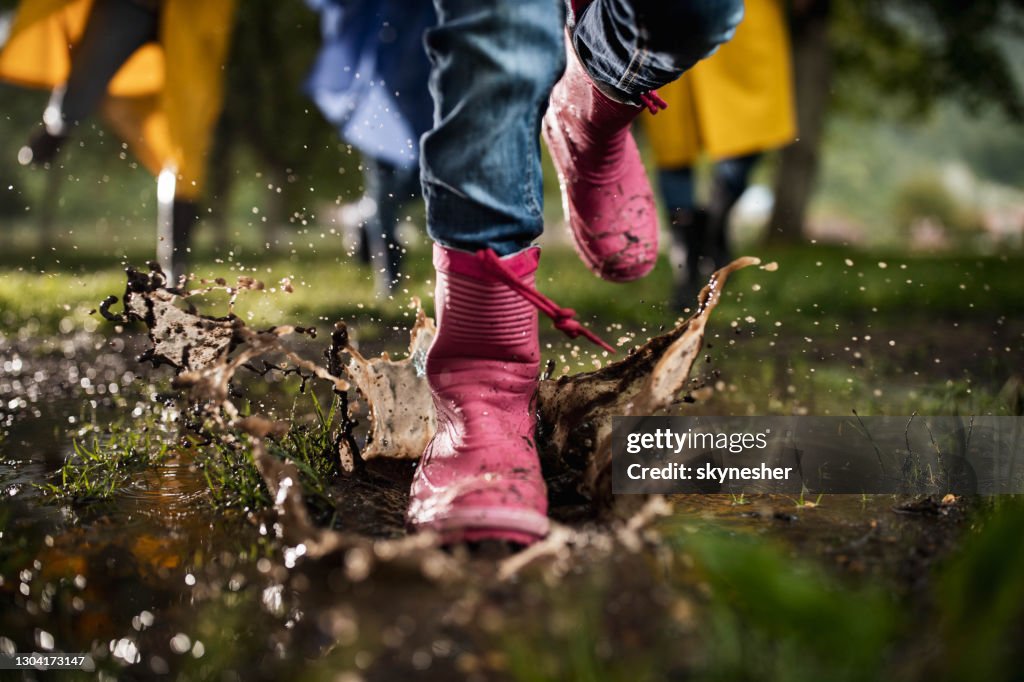 Unrecognizable child running through muddy puddle in nature.