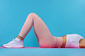 Woman doing exercises with resistance bands at home. Cropped shot of a young fit woman exercising on the floor. Workout at home, quarantine, body care concept on blue background