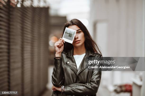 linda hembra cubriendo la cara con fotografía polaroid - chaqueta de ante fotografías e imágenes de stock