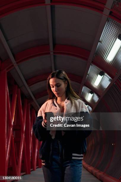 a young woman walks with her phone across a red bridge at night - one kid one world a night of 18 laughs stockfoto's en -beelden