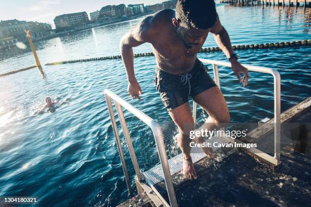 young multiracial man coming out of cold water after swim in denmark - people coming of age purify with icy water in tokyo stockfoto's en -beelden