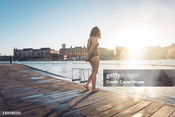 fit woman standing alone on dock before swim in copenhagen, denmark - morning swim stockfoto's en -beelden