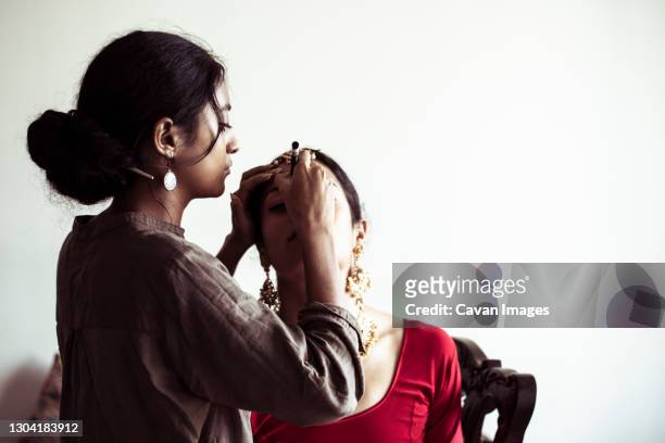 young indian woman applies make up to bride before indian wedding - indian bridal makeup stock pictures, royalty-free photos & images
