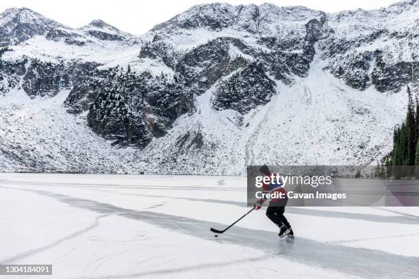 hockey player ice skating on frozen lake near snowy mountain - outdoor ice hockey stock pictures, royalty-free photos & images
