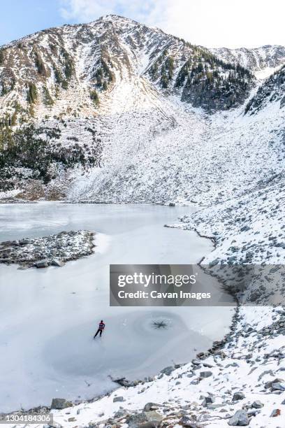 drone view of hockey player skating on frozen lake near snowy mountain - pond hockey stock pictures, royalty-free photos & images