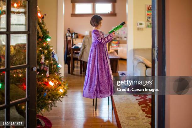 a small child in a long princess dress stands on chair with toy gun - furious 7 foto e immagini stock