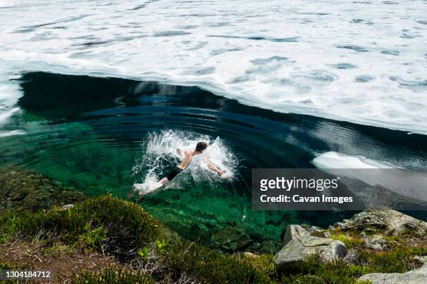 unrecognizable man plunging in frozen ice covered clear cold lake - ice bath stock pictures, royalty-free photos & images