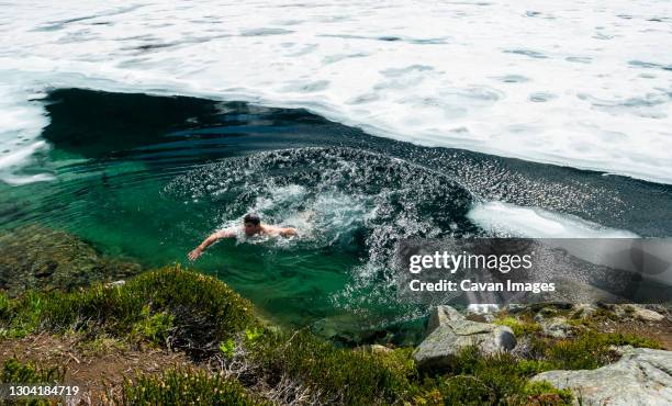 man swims out of cold water in a frozen lake on sunny day in mountains - nieuwjaarsduik stockfoto's en -beelden