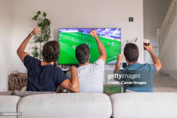 three friends watching a soccer game at home drinking beer - soccer stockfoto's en -beelden