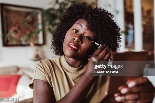 mature afro woman applying mascara at home - schminken stock-fotos und bilder