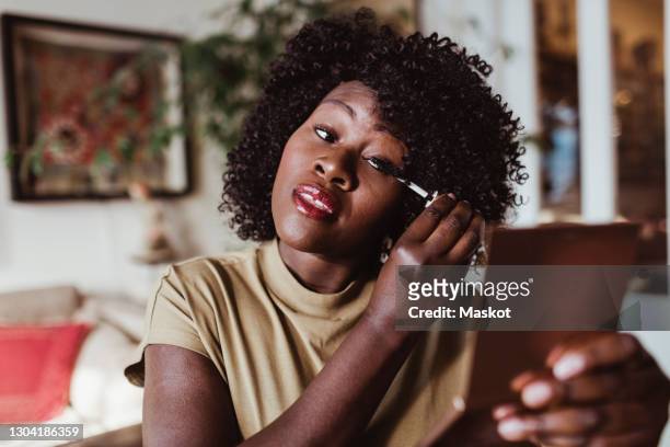 mature afro woman applying mascara at home - trucco per il viso foto e immagini stock