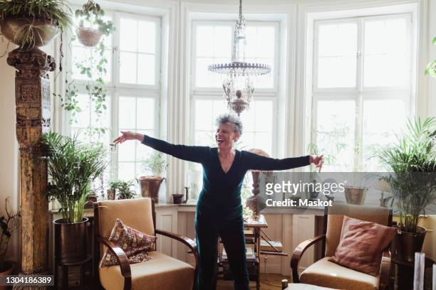 happy senior woman dancing with arms outstretched in living room at home - senior women dancing stock pictures, royalty-free photos & images