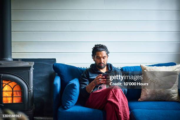 asian man sitting by fire checking mobile phone - wood burning stove fotografías e imágenes de stock