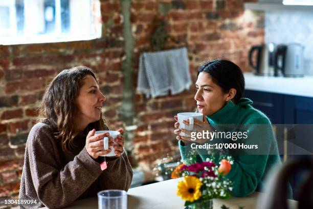 two women enjoying hot drink having conversation - vriendin stockfoto's en -beelden